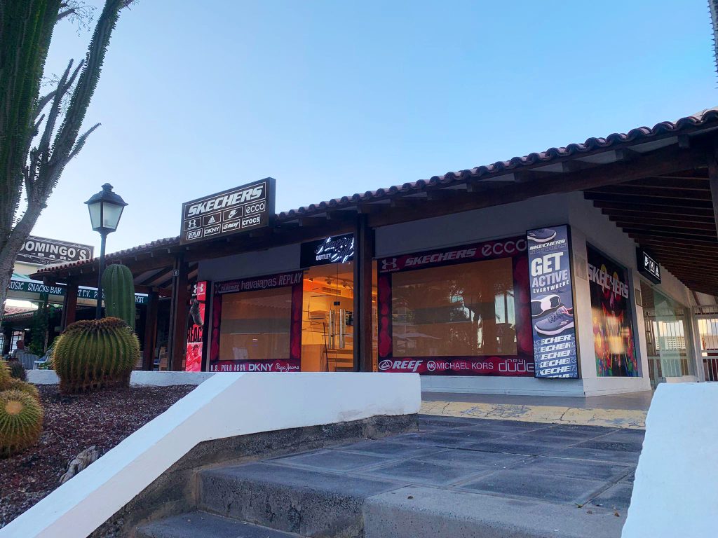 entrada principal de una tienda deportiva donde se ven diferentes casa de luz con publicidad y vinilos instalados en los vidrios de su fachada