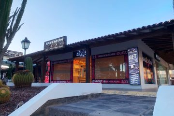 entrada principal de una tienda deportiva donde se ven diferentes casa de luz con publicidad y vinilos instalados en los vidrios de su fachada